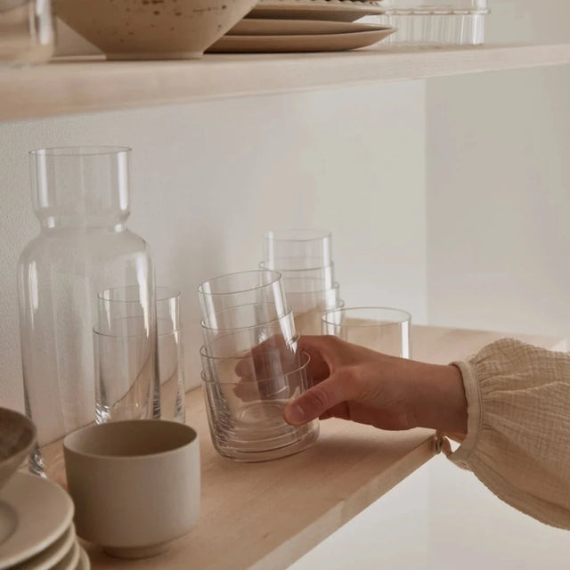 Aarke Nesting Glasses ineinander gestapelt auf einem Holzregal neben Karaffe und Geschirr