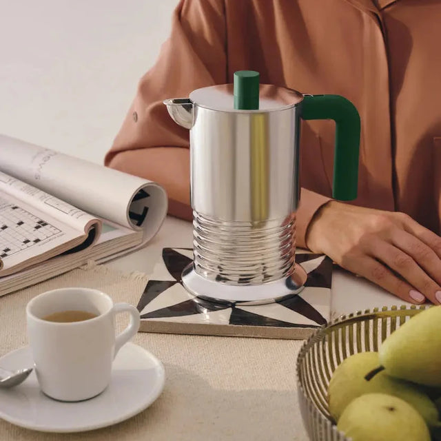 Alessi Vite Espressokocher in Aluminium mit grünem Griff auf dem Esstisch neben einer Espressotasse