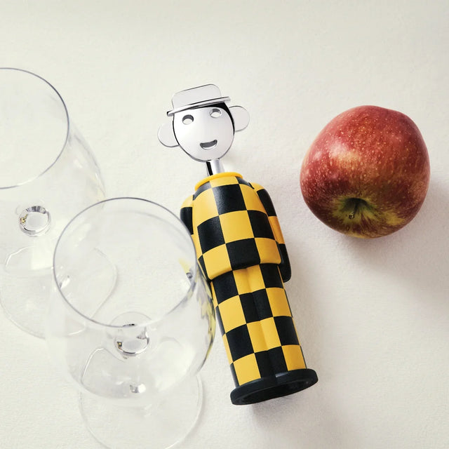 Alessi Korkenzieher Alessandro M. im Dekor Giallo e Nero neben Weingläsern und einem Apfel