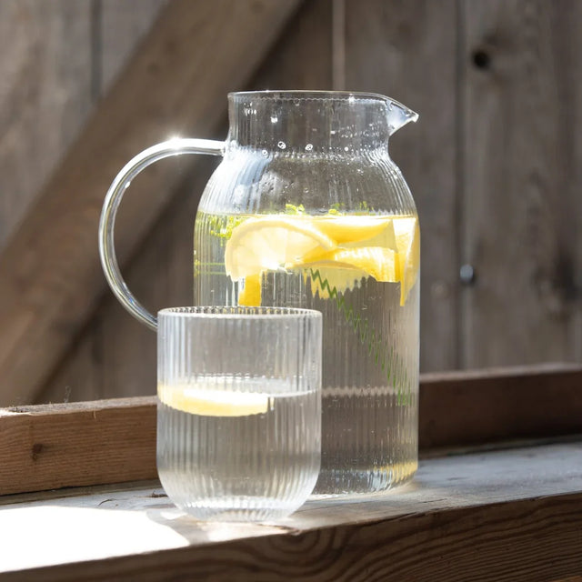Wasserkaraffe aus Glas mit Zitrone und geriffeltem Trinkglas auf dem Tisch, Wikholm Form